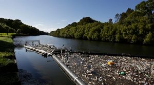 A litter boom filled with rubbish in its arm sits on a still blue river