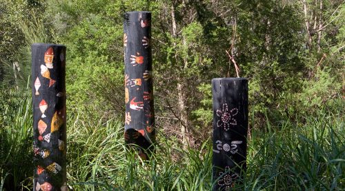 Three black Aboriginal totem poles with orange and red markings including hand prints