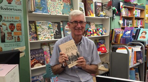 Ian Tyrrell sitting in a bookstore holding his book River Dreams