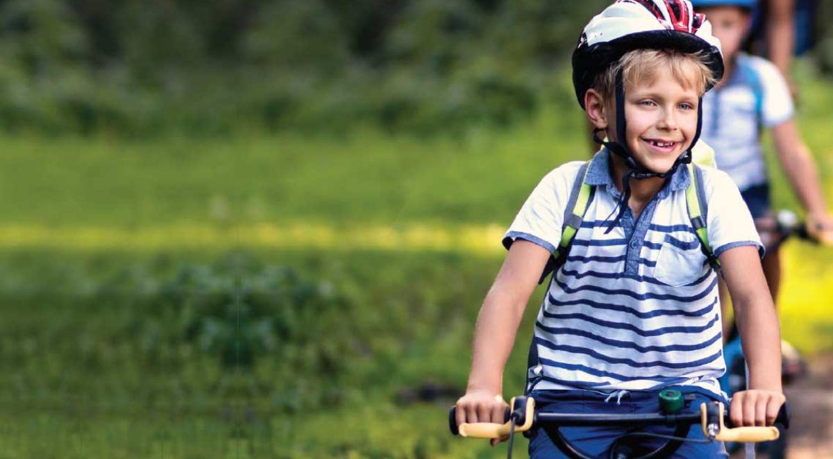 Photo of a young boy cycling beside greenery