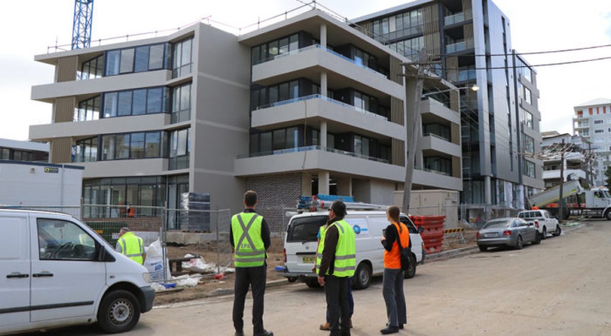 Council rangers wearing flouro yellow vests inspect fencing around an apartment building site